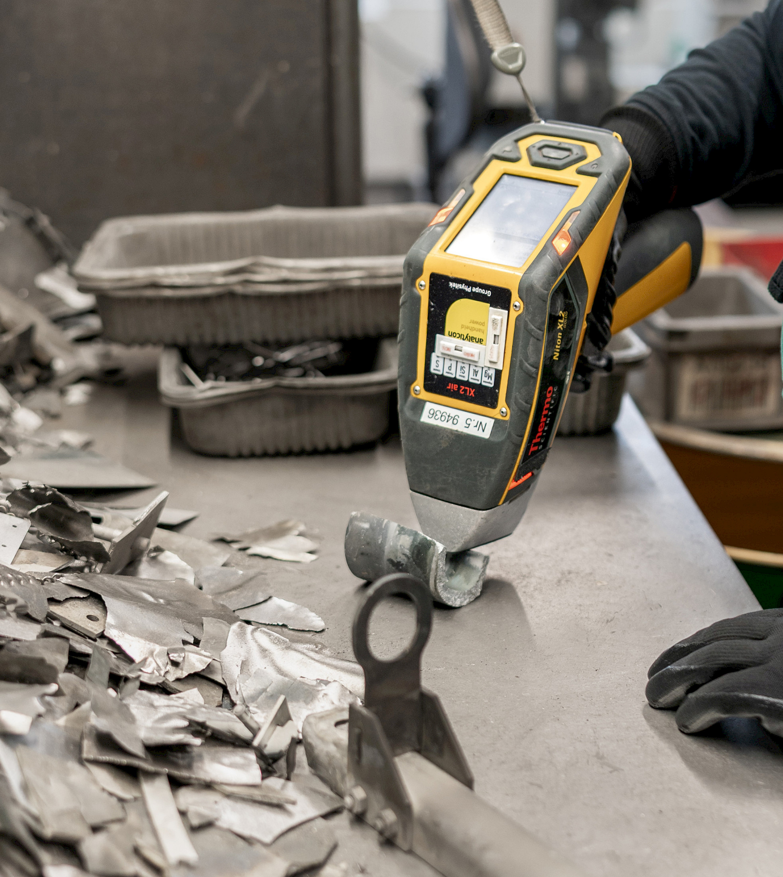 Hand hält Analysegerät über Metallteile auf einem Tisch.